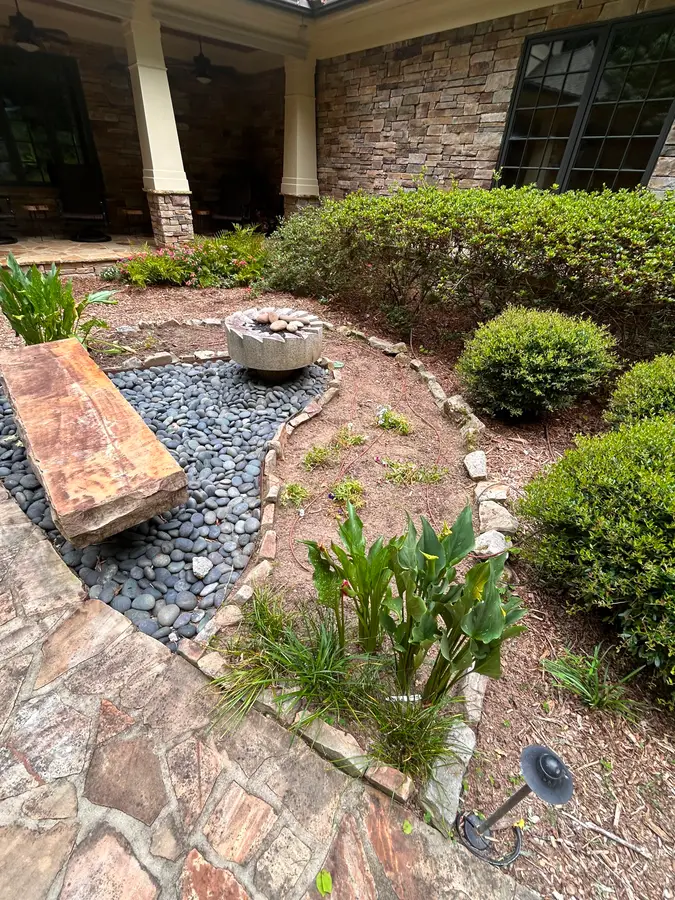 Bubbling-boulder water feature set in a river-rock dry creek with a stone bench and plantings