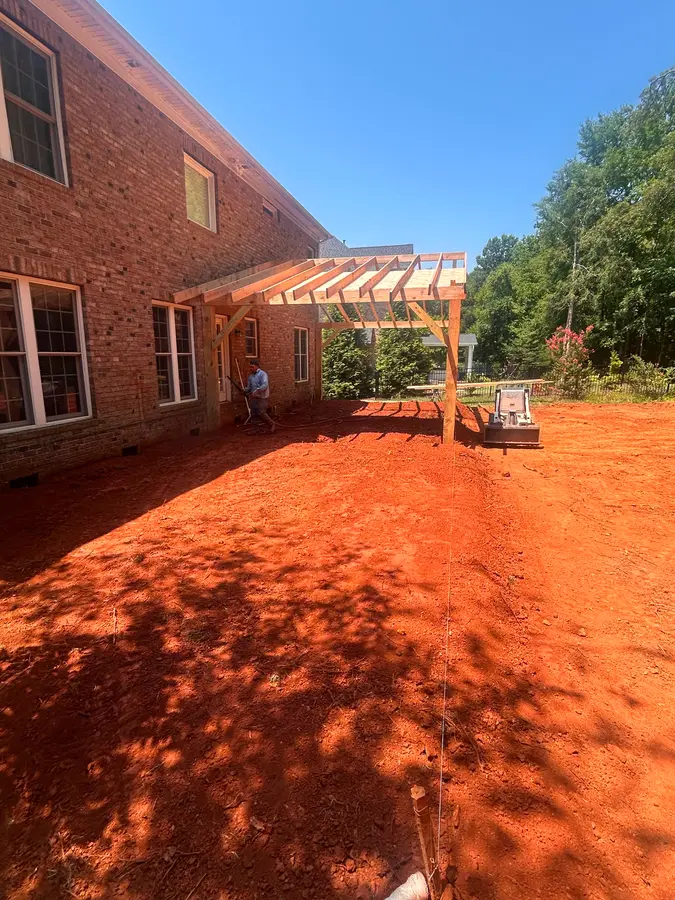 Custom cedar pergola under construction over a freshly graded backyard at a brick South Charlotte home
