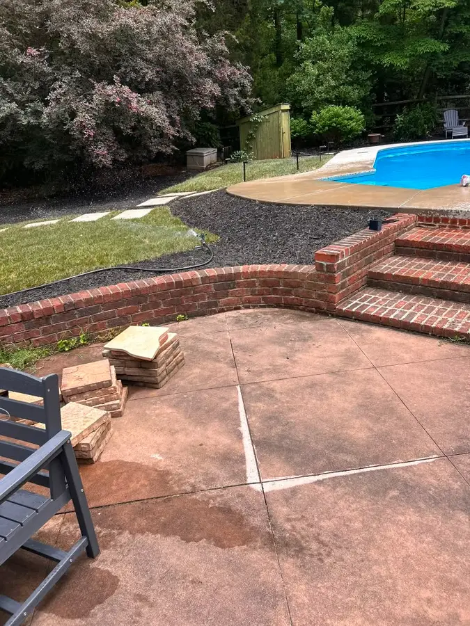 Curved brick retaining wall, steps, and stamped-concrete patio beside a backyard pool in South Charlotte