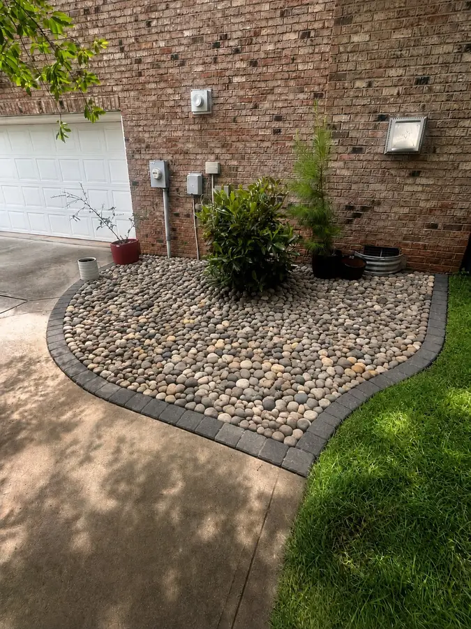 River-rock landscape bed edged with a charcoal paver border against a brick home